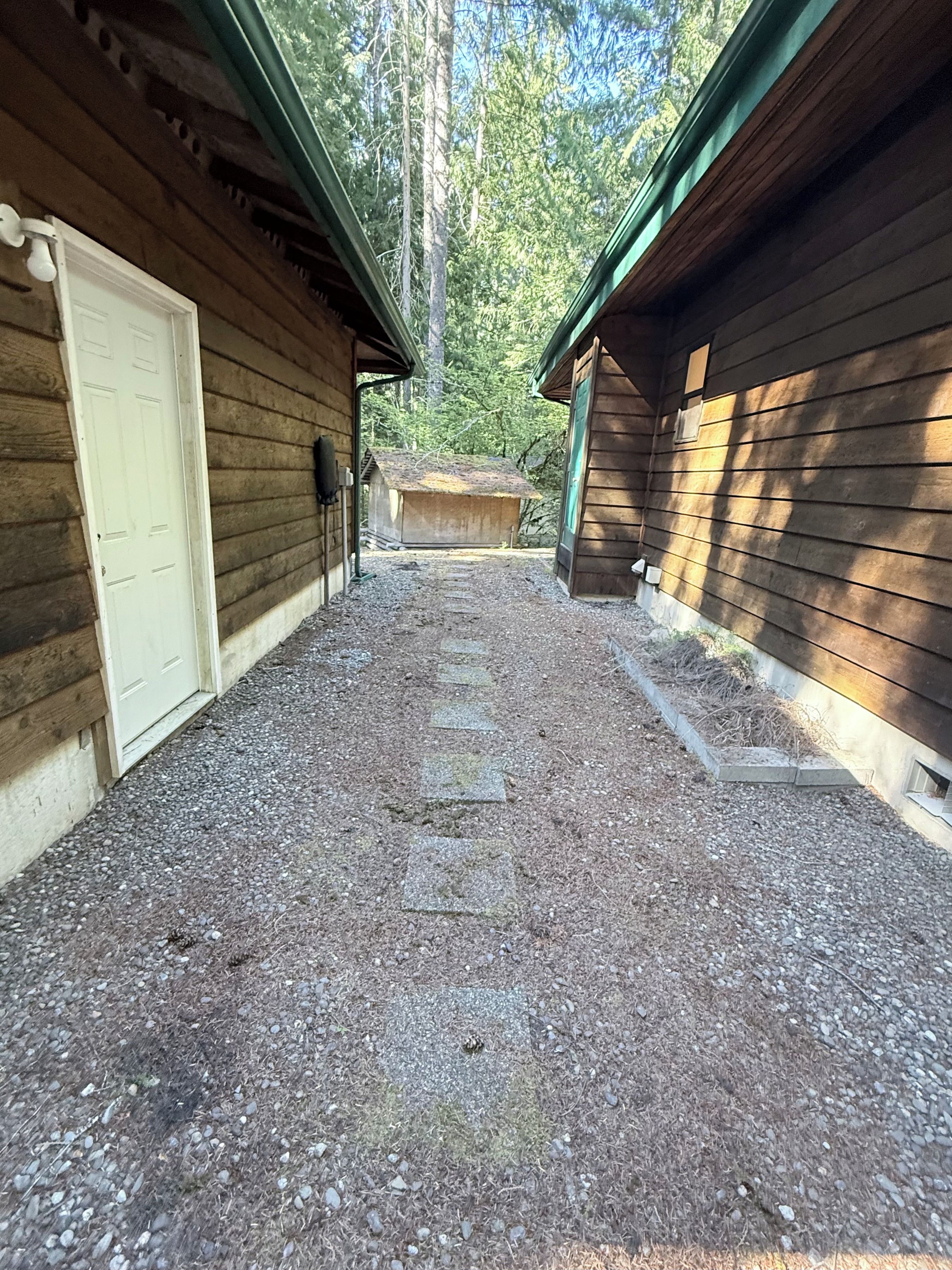 A gravel pathway leading to a wooden cabin with a door on the left and a window on the right.