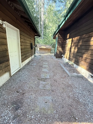 A gravel pathway leading to a wooden cabin with a door on the left and a window on the right.