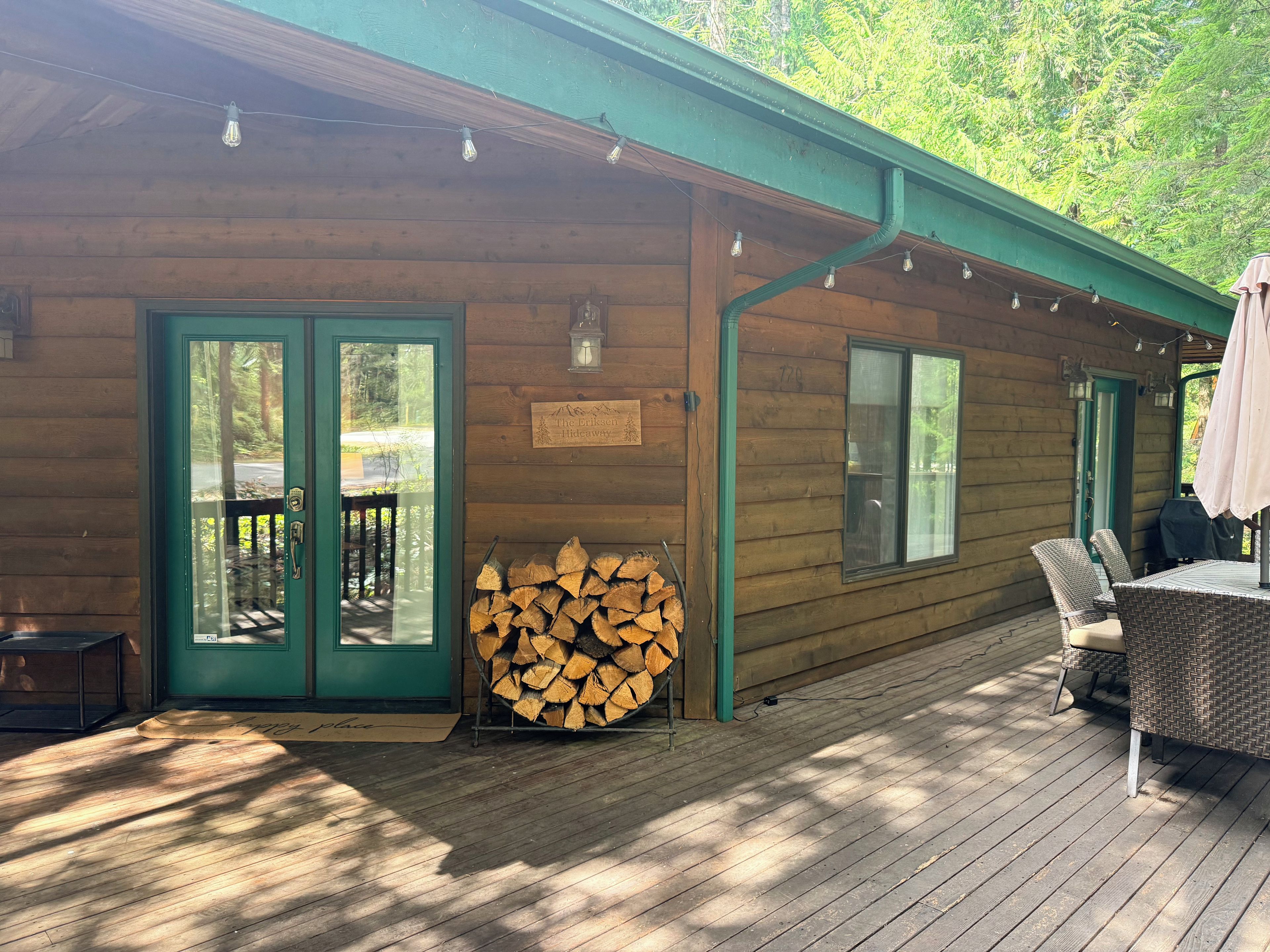 A wooden cabin with a covered deck, a stack of firewood, and a sign indicating it's a hideaway.