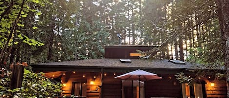 Un chalet rustique doté d’un porche, entouré d’une forêt dense.