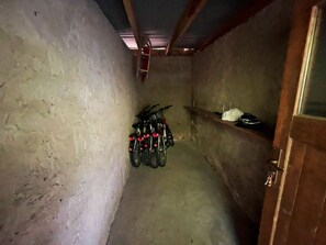 Ein schmaler Korridor mit Betonwänden, einer Holztür rechts und einem Fahrradständer an der linken Wand.