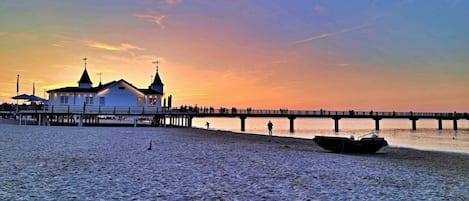 A pier extending into a calm body of water with a building at the end, likely a pierhead house, and a boat moored nearby.
