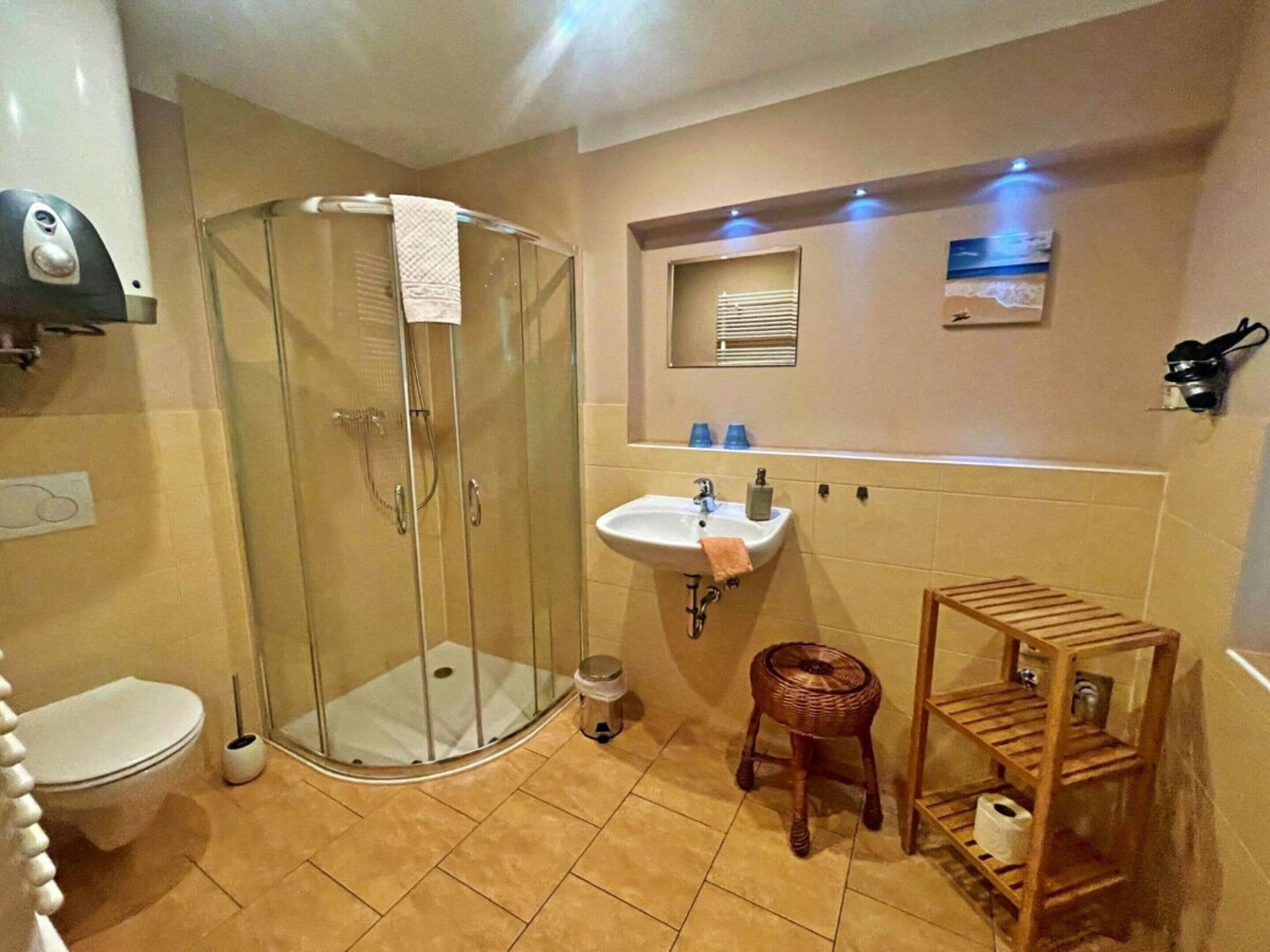 Une salle de bain avec une douche à parois de verre, des toilettes, un lavabo et une petite étagère en bois.