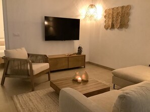 Ein Wohnzimmer mit einem an der Wand befestigten Flachbildfernseher, einem Couchtisch aus Holz mit Kerzen und zwei Sofas.