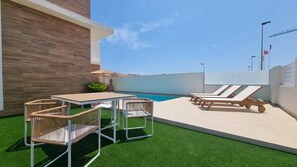 Eine Dachterrasse mit Pool, Liegestühlen und einem Tisch mit Stühlen.