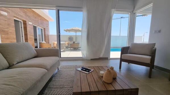 A modern living room with a sofa, armchair, and a coffee table with remote control and vases. - Brand new modern villa in Ibiza style with private pool and safe neighbourhood (San Javier)