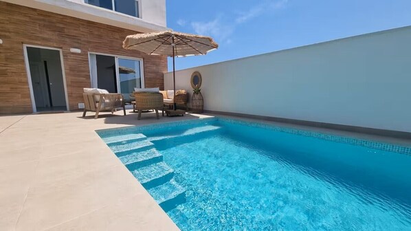 Ein Pool mit Liegestühlen und Sonnenschirm, umgeben von einem Gebäude im modernen Stil.