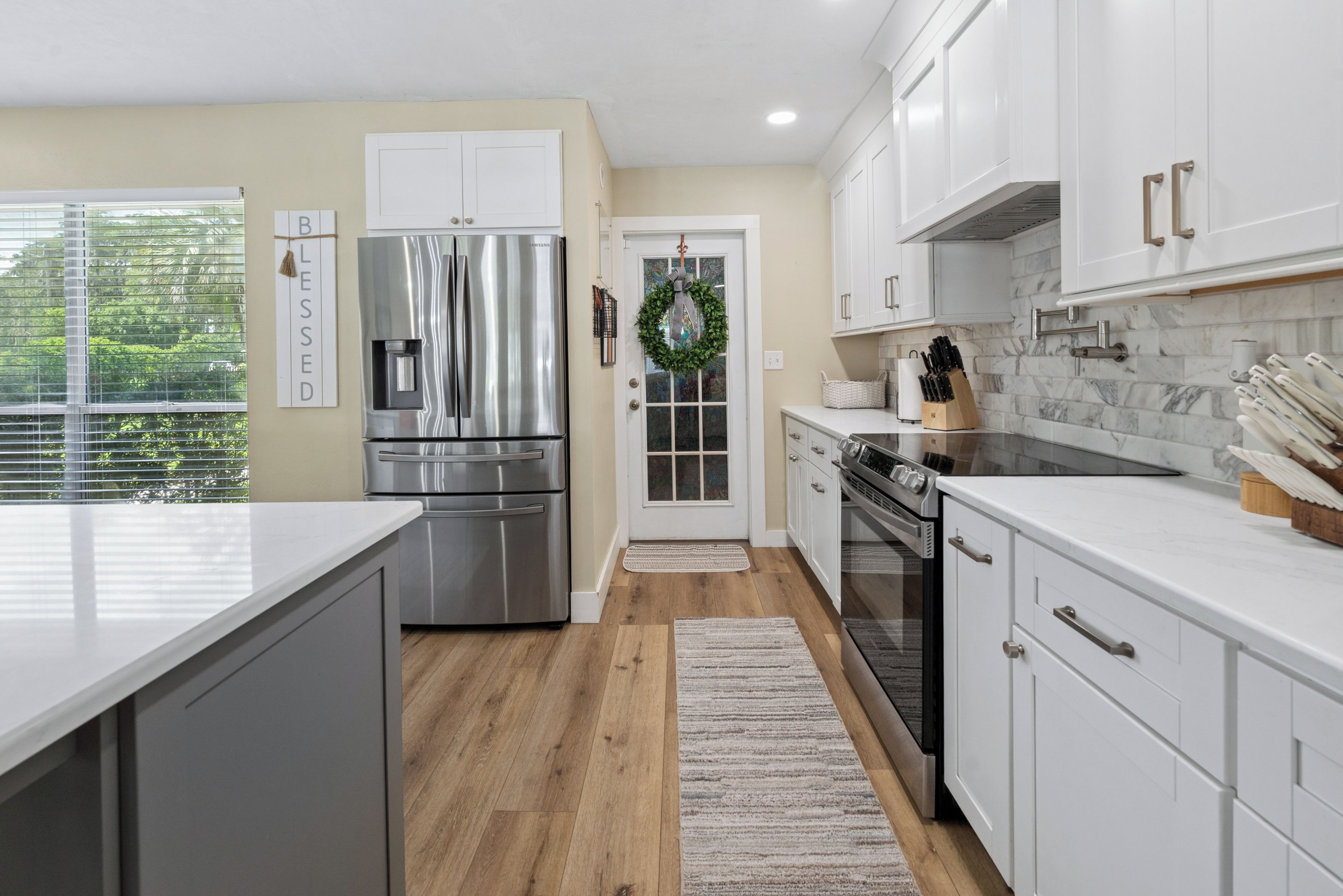 A modern kitchen with stainless steel appliances, white cabinetry, and a view of greenery outside.