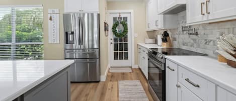 A modern kitchen with stainless steel appliances, white cabinetry, and a view of greenery outside.