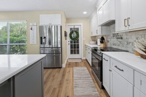 A modern kitchen with stainless steel appliances, white cabinetry, and a view of greenery outside. - Lake Santa Fe canal front pool home with private boat ramp and dock. (Melrose)