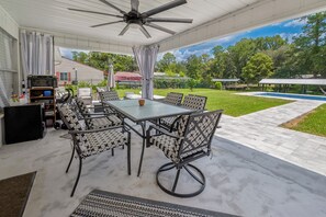 An outdoor patio with a table and chairs, a ceiling fan, and a view of a swimming pool and greenery. - Lake Santa Fe canal front pool home with private boat ramp and dock. (Melrose)