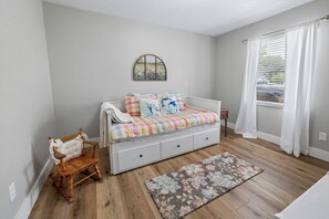 Une chambre à coucher avec un lit, une chaise, un tapis et une fenêtre avec des rideaux.