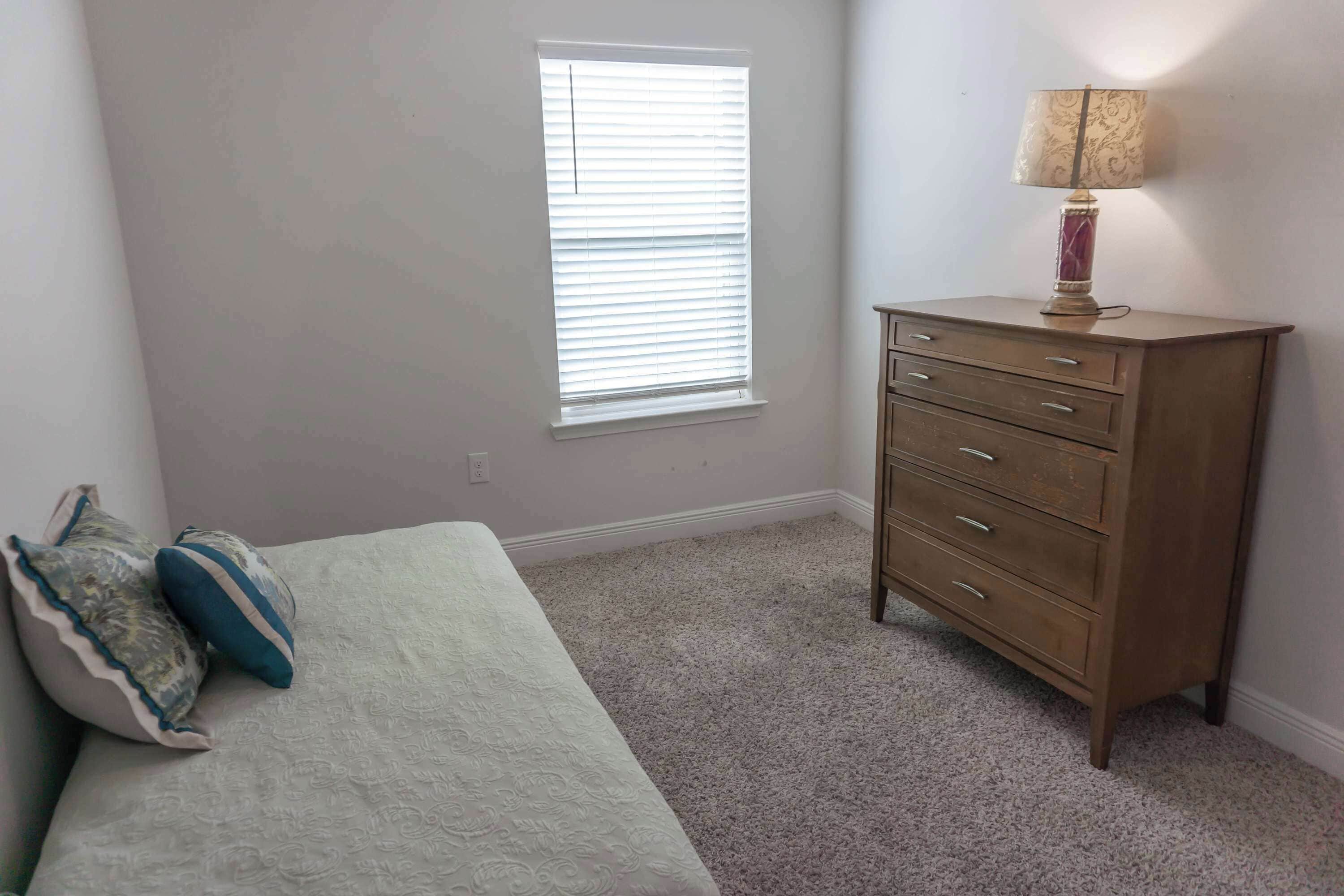 Un dormitorio con una cama, un tocador, una lámpara y una ventana.