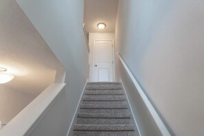 Eine enge Treppe mit Teppichstufen, weißen Wänden und einer Tür am oberen Ende.