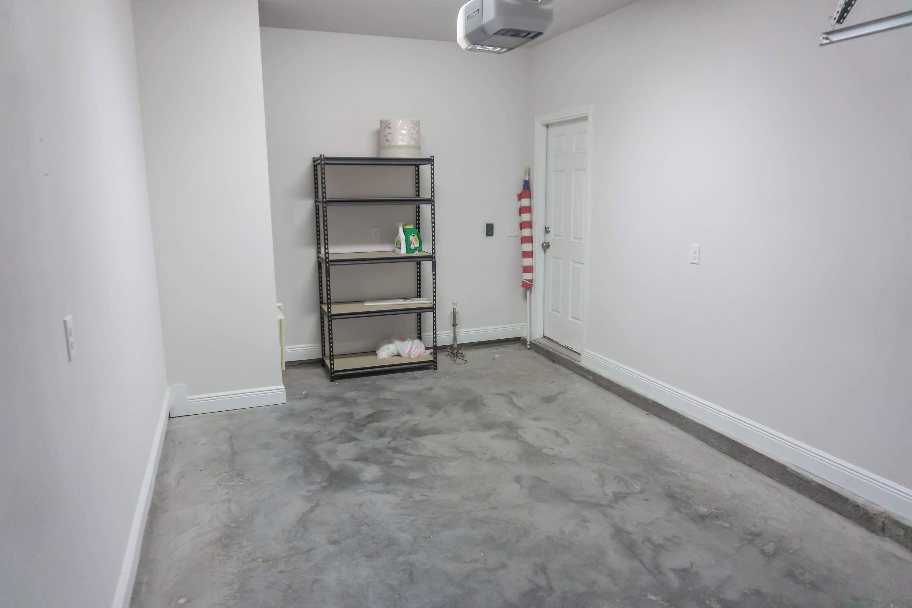 A room with a concrete floor, a metal shelving unit against the wall, and a white door with a striped curtain.