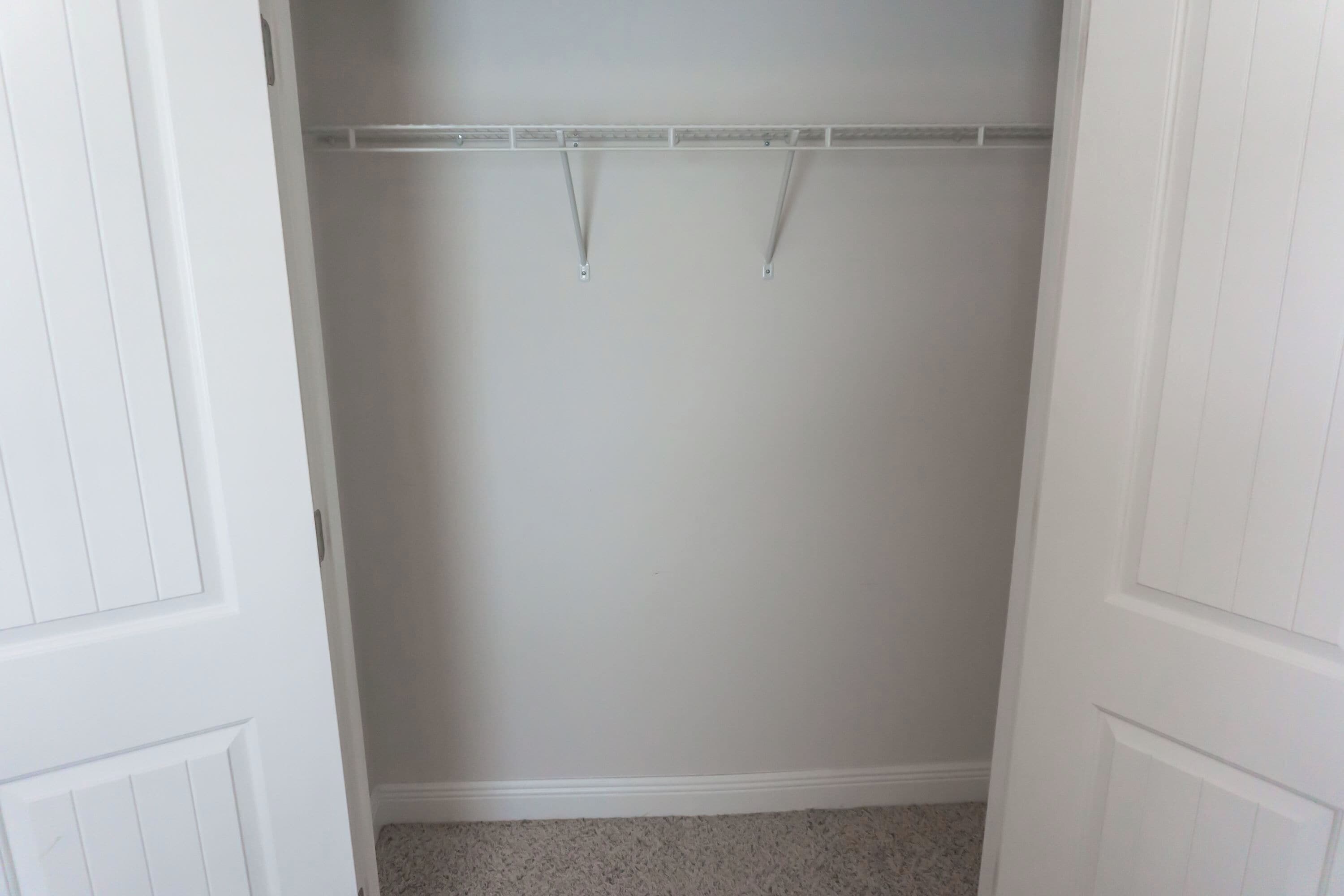 A closet with a hanging rod, white walls, and a carpeted floor.