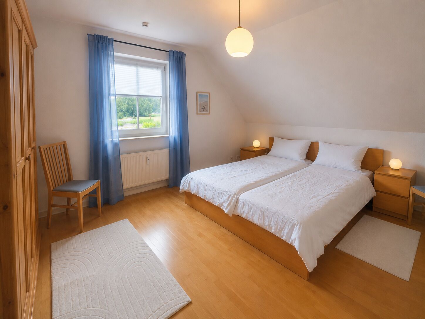 Ein Schlafzimmer mit einem Doppelbett, zwei Nachttischen, einem Sessel, einem Fenster mit Vorhängen, einem Heizkörper und einer Hängeleuchte.