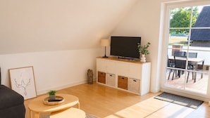 A modern living room with a sofa, a round table, a flat-screen TV, and a sliding glass door leading to an outdoor area. - Meerbeck Vacation Rental (Meerbeck)