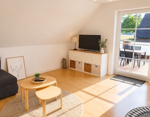 A modern living room with a sofa, a round table, a flat-screen TV, and a sliding glass door leading to an outdoor area. - Meerbeck Vacation Rental (Meerbeck)