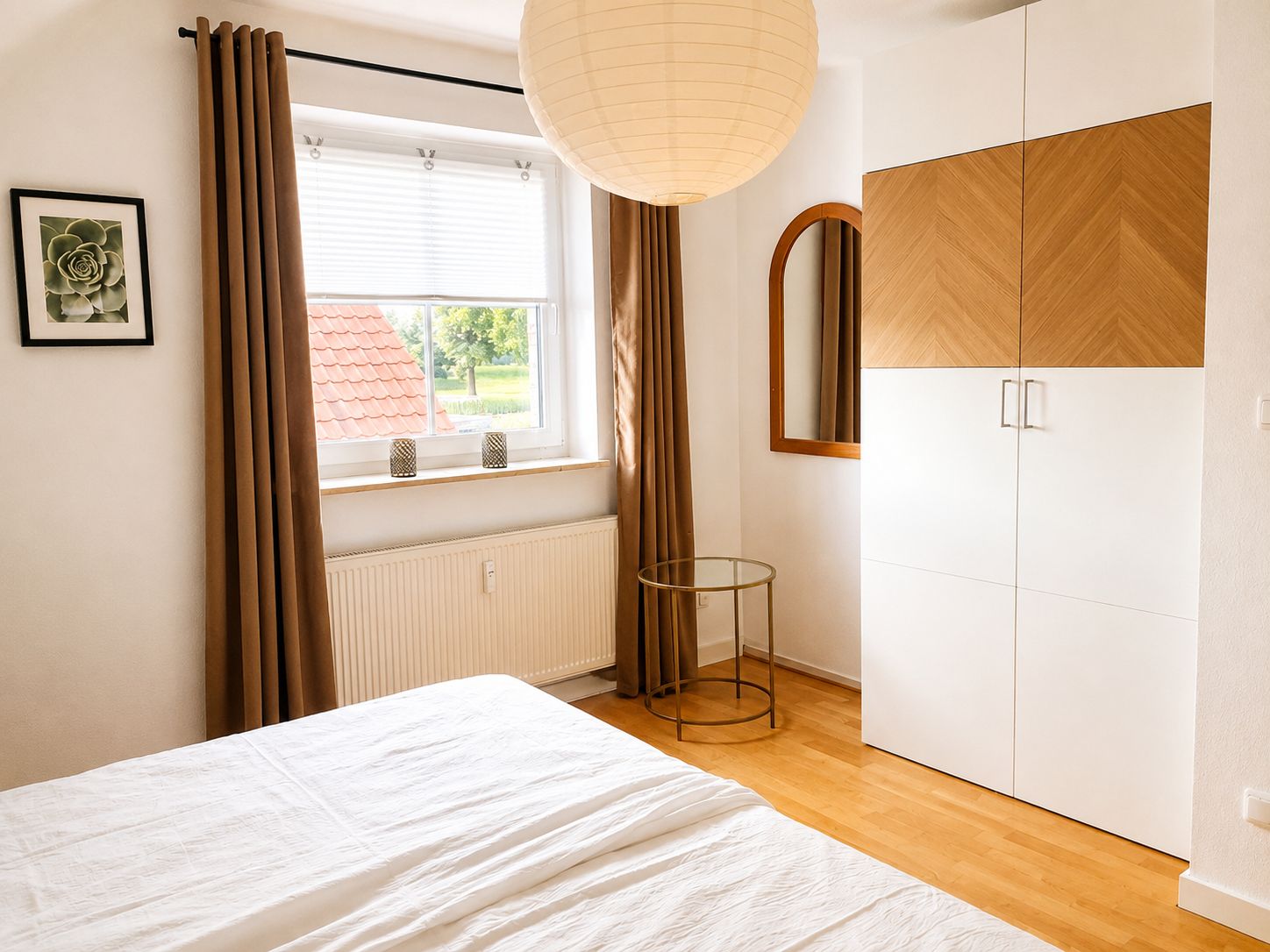 A bedroom with a bed, a window with curtains, a radiator, a bedside table, and a wardrobe.