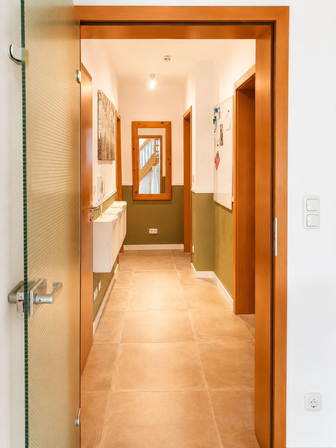 Un corridoio con una porta in legno, un lavandino bianco e uno specchio appeso al muro.