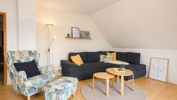 Ein stilvolles Wohnzimmer mit Sofa, Sessel und Couchtisch, ausgestattet mit einem großen Fenster und hoher Decke.
