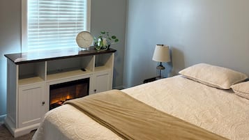 A bedroom with a bed, a nightstand, a lamp, a clock, and a fireplace.