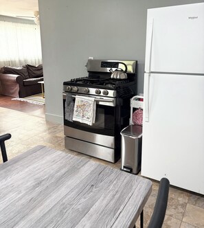 A kitchen with a stainless steel stove, a refrigerator, and a dining table.