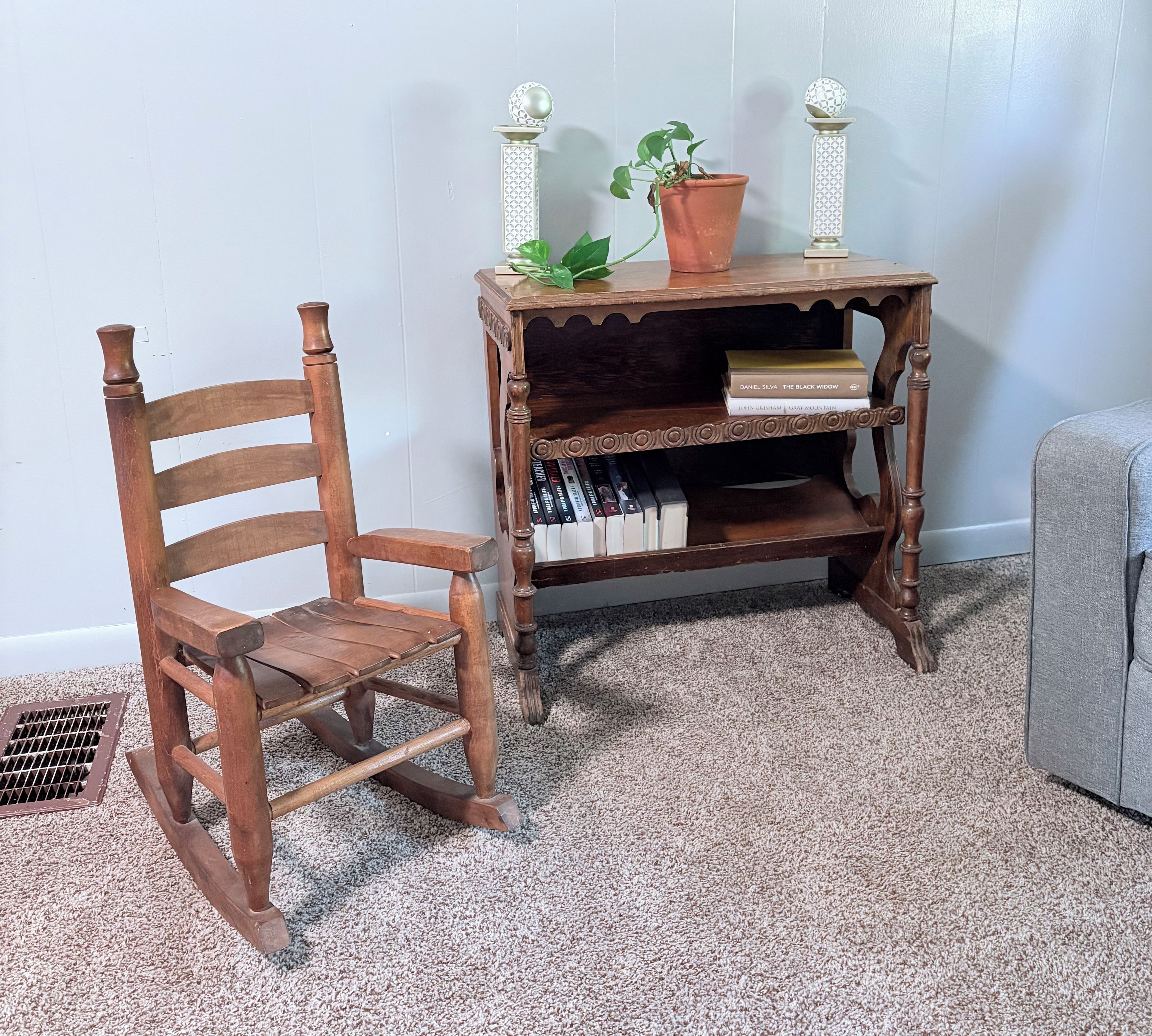 Una mecedora de madera y una mesita auxiliar con libros y una planta en maceta.