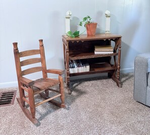 A wooden rocking chair and a wooden side table with books and a potted plant.