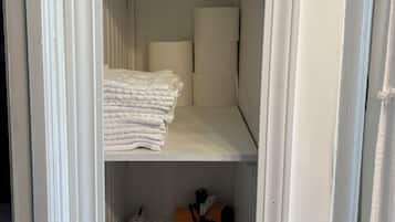 A closet with neatly folded towels, a shelf with rolled towels, and toiletries including a water bottle, toothbrushes, and a box of tissues.