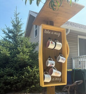 A wooden sign with the text 'Take a mug' and several mugs hanging from it.