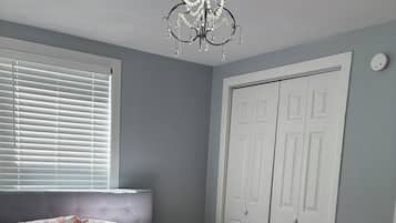 Un dormitorio con una cama, un ventanal con persianas, un armario blanco y una araña.