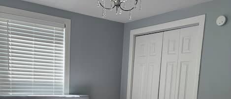 Un dormitorio con una cama, un ventanal con persianas, un armario blanco y una araña.