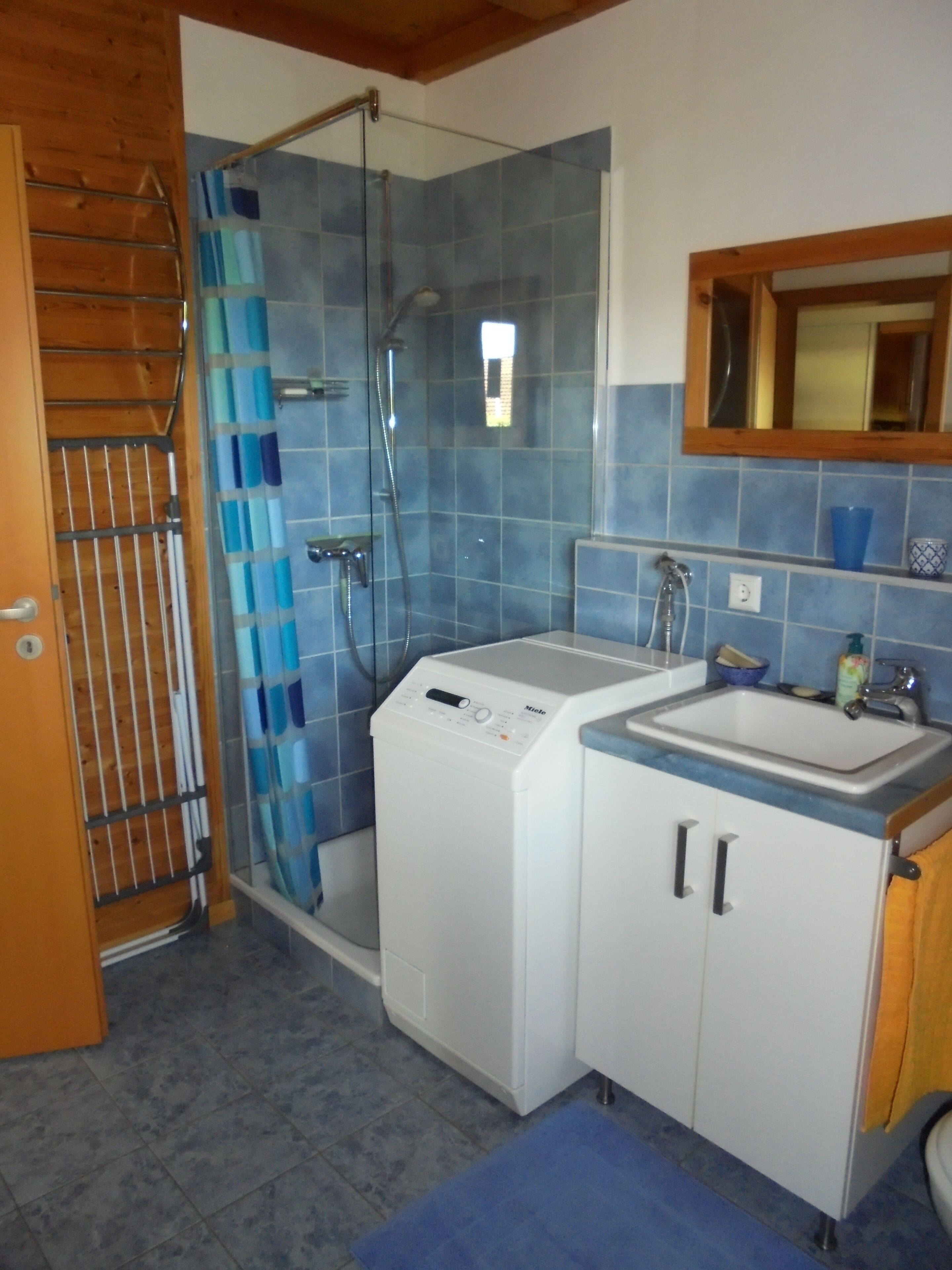 A bathroom with a glass-enclosed shower, a washing machine, and a sink with a mirror above it.