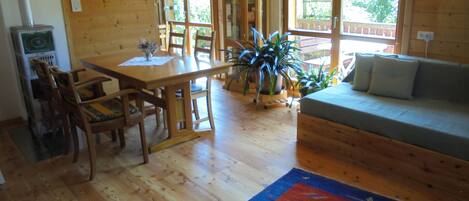 A wooden interior with a dining table, chairs, a sofa, and a large window.