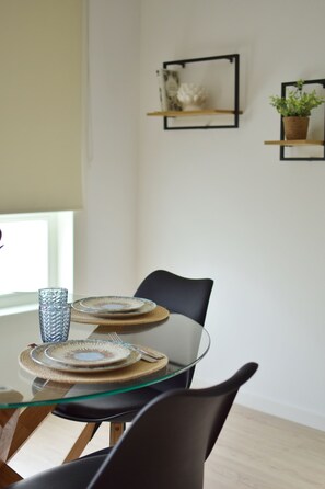A dining area with a glass table, two chairs, and a window with blinds. - DULCE ESTRELA APARTMENTS: 5 minutes from downtown, spectacular views (Tui)