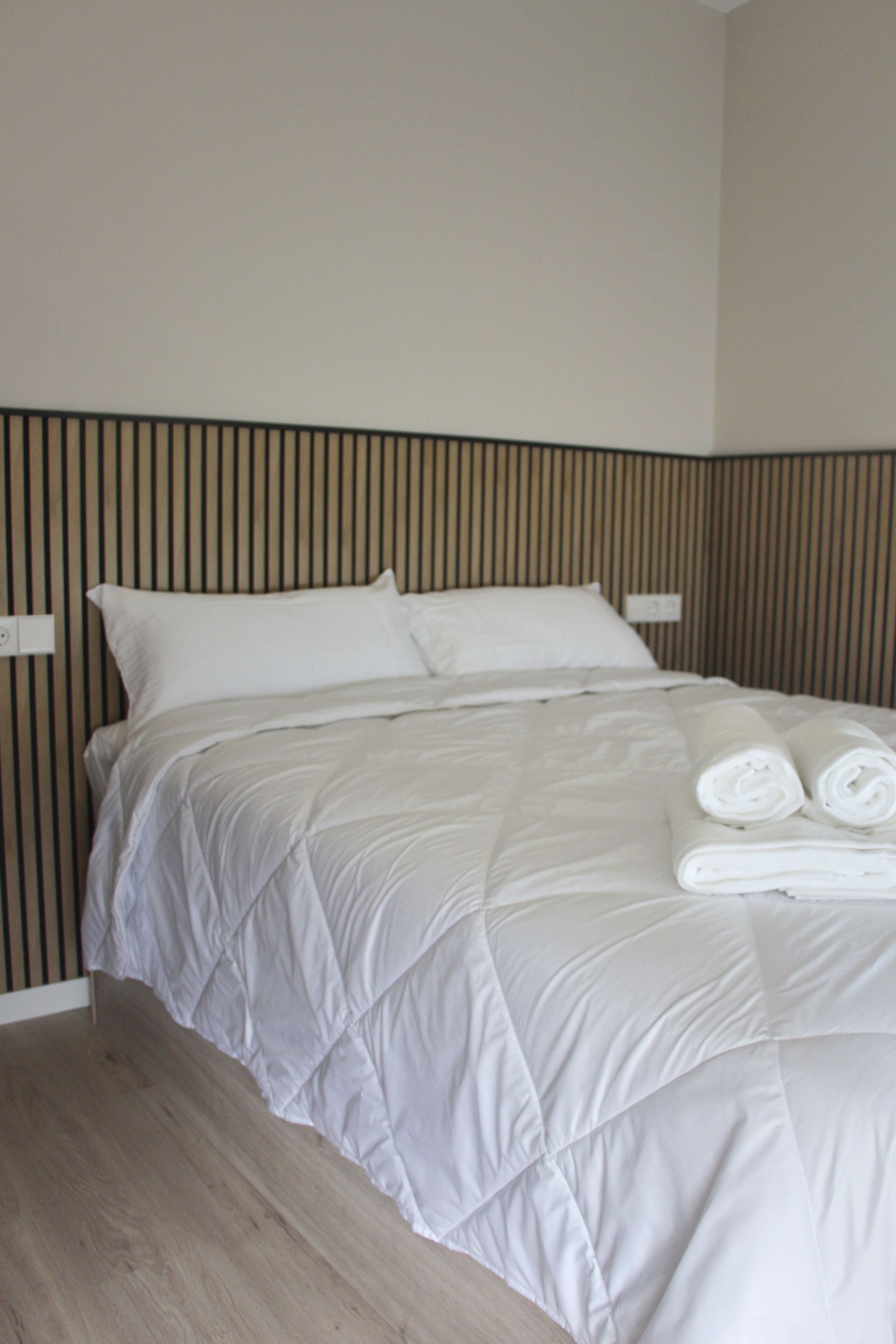 A bed with a white quilted bedspread and two rolled towels on it.