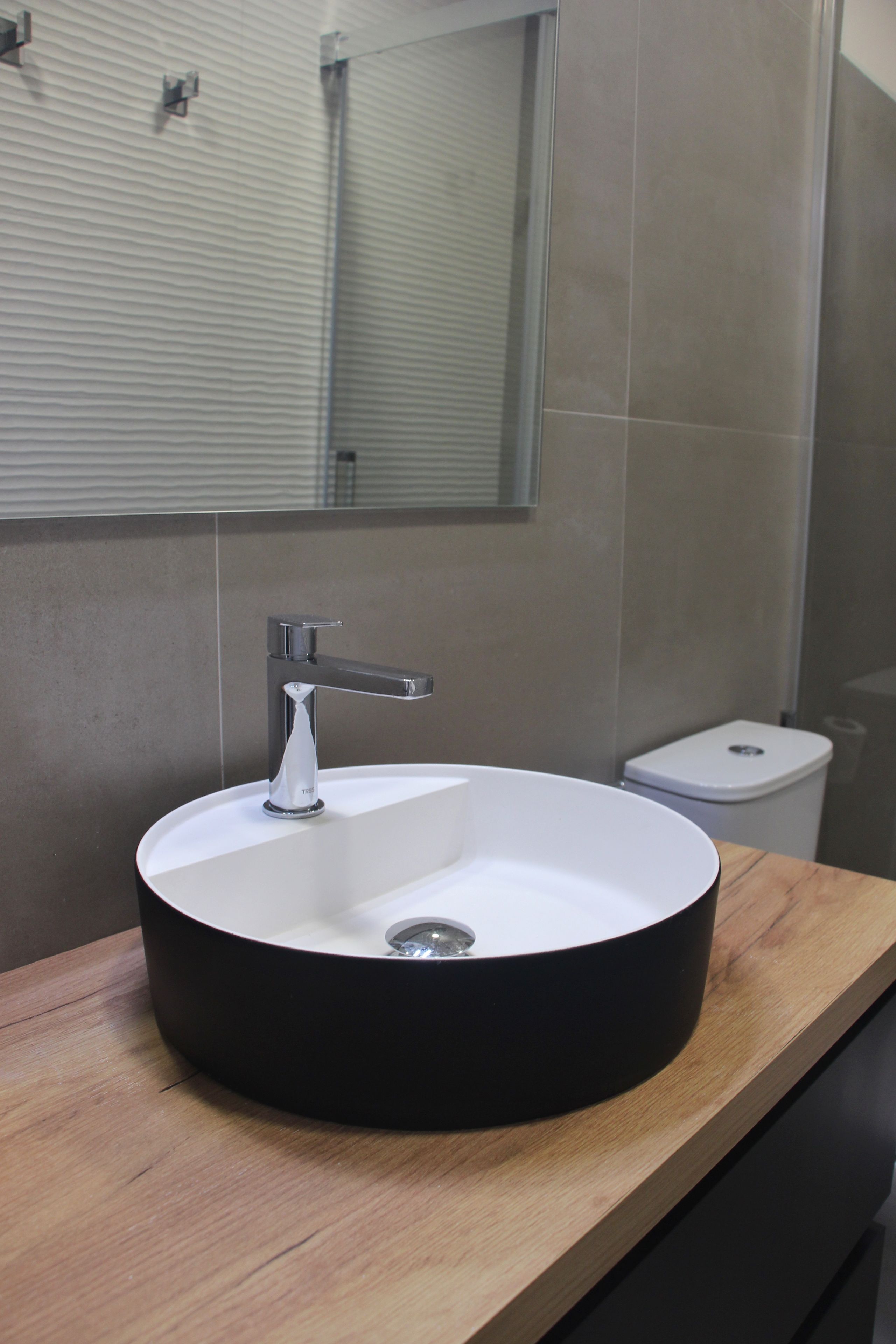 A bathroom with a round sink, a mirror, and a toilet.