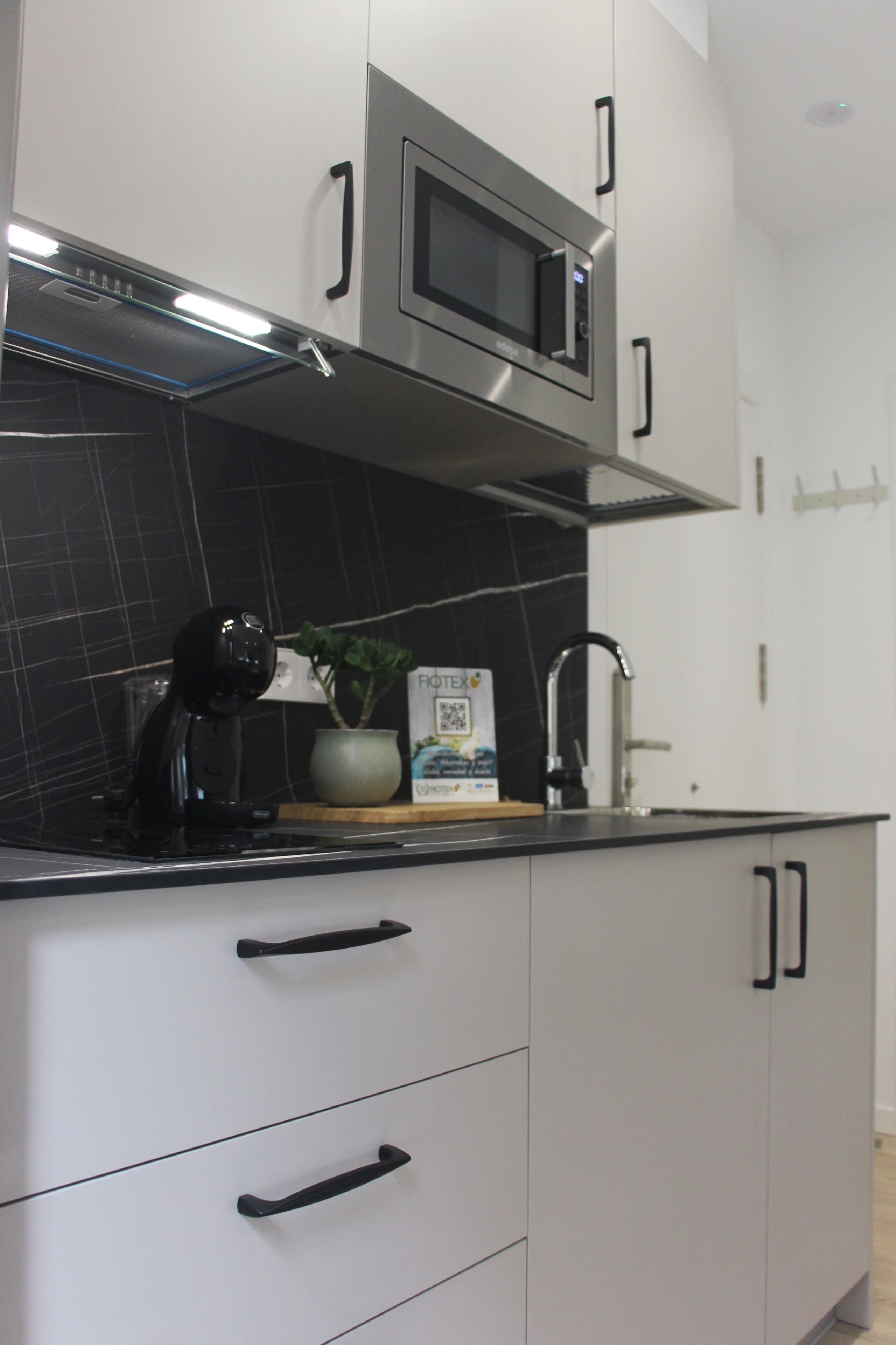Een moderne keuken met een magnetron, fornuis en een zwart betegelde spatwand.