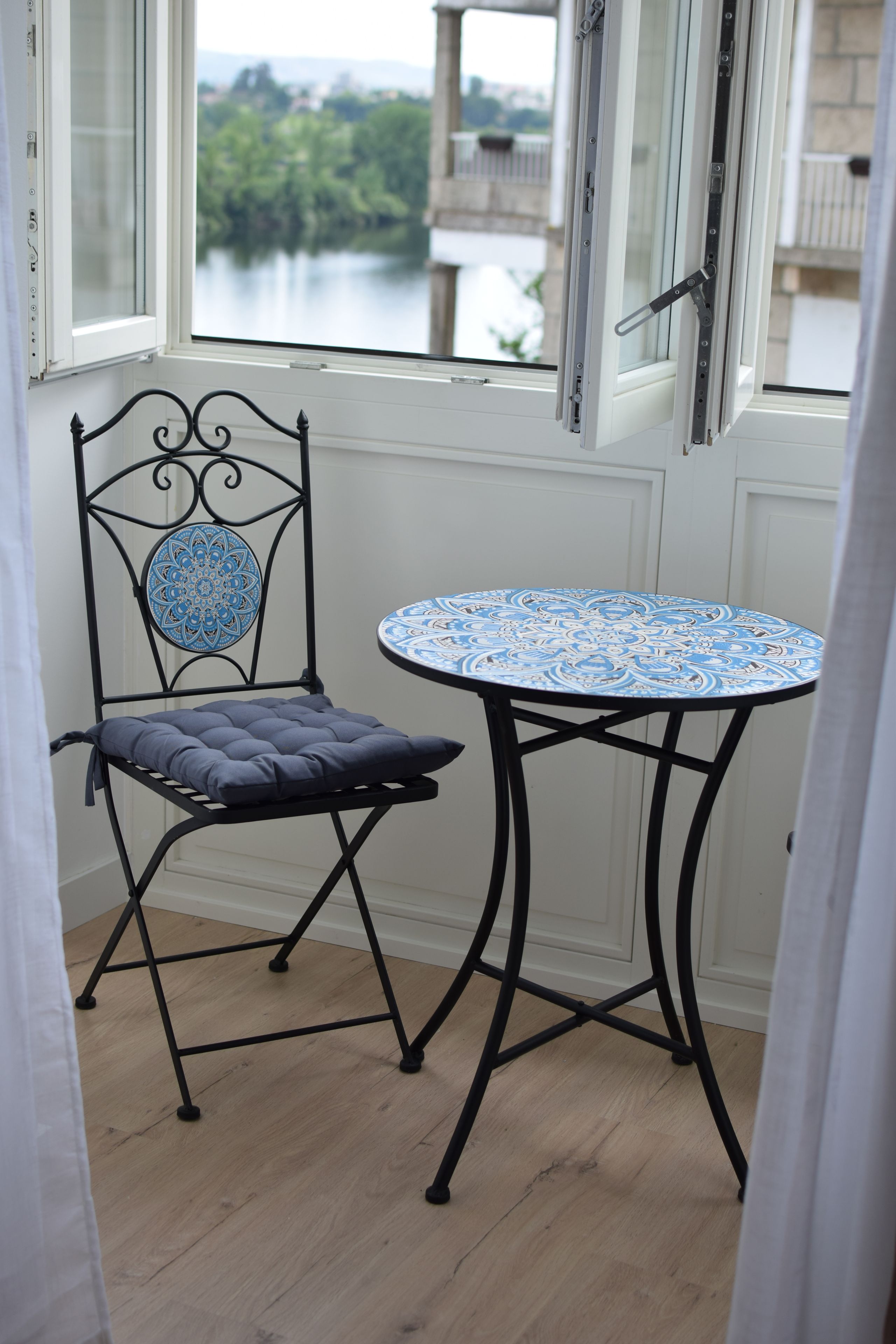 Quarto com vista para um lago, uma mesa com toalha de padrão e uma cadeira com almofada.