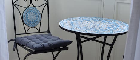 A room with a view of a lake, a table with a patterned tablecloth, and a chair with a cushion.