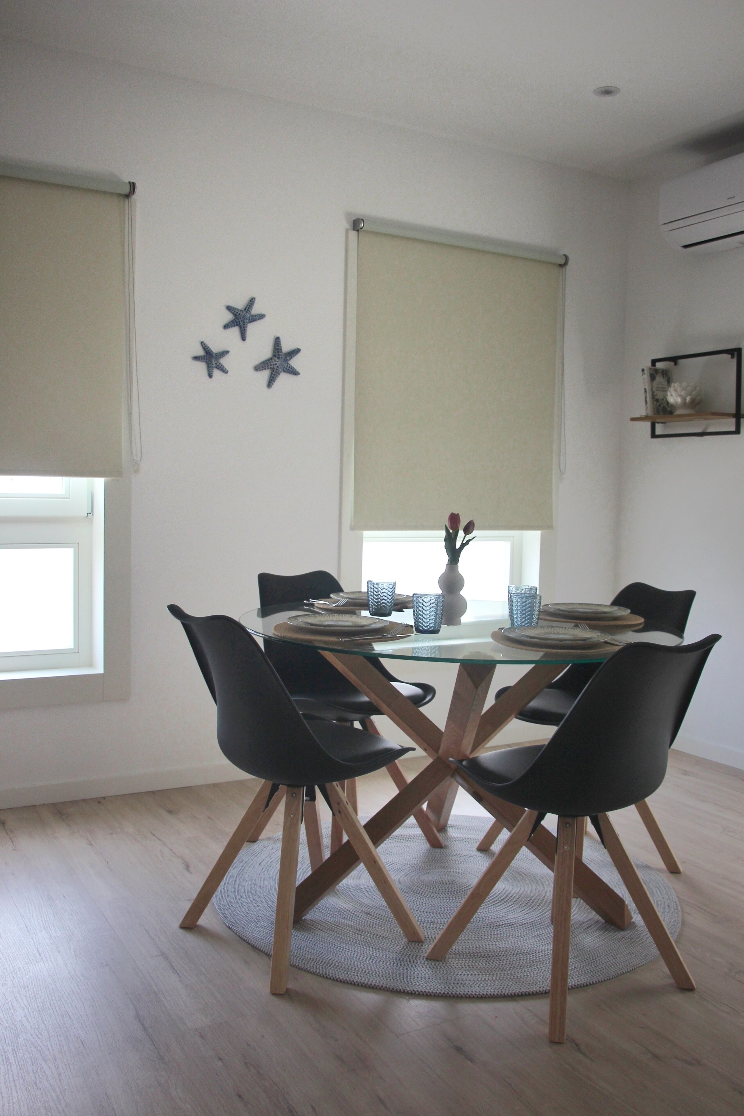 Een eetruimte met een ronde glazen tafel, zwarte stoelen en een centrale vaas.