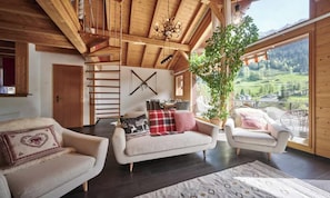 A spacious living area with a wooden ceiling, a staircase, and a large window offering a view of a green landscape. - TRADITIONAL SWISS CHALET WITH PANORAMIC LAUTERBRUNNEN VIEWS (Lauterbrunnen)