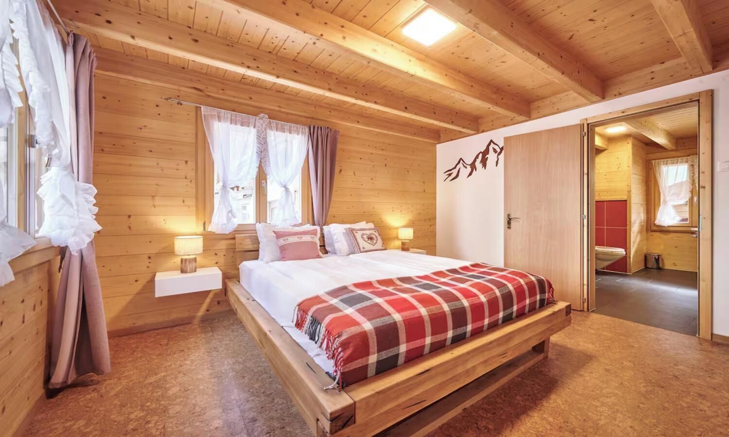 Ein Schlafzimmer einer Holzhütte mit einem Bett, Nachttischen und einem Fenster mit Vorhängen.