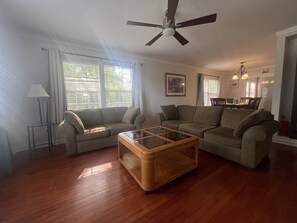 Ein Wohnzimmer mit zwei Sofas, einem Couchtisch, einem Deckenventilator und einem Essbereich im Hintergrund.