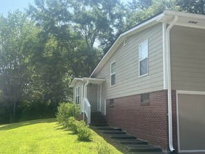 A two-story house with a brick foundation and white siding, a front porch, and a garage. - Charming 3-bedroom house with AC in Buford (Buford)
