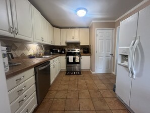 A kitchen with white cabinets, stainless steel appliances, a tiled floor, and a ceiling light. - Charming 3-bedroom house with AC in Buford (Buford)