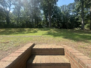 A brick structure with steps leading up to a flat area, surrounded by a grassy field and trees. - Charming 3-bedroom house with AC in Buford (Buford)