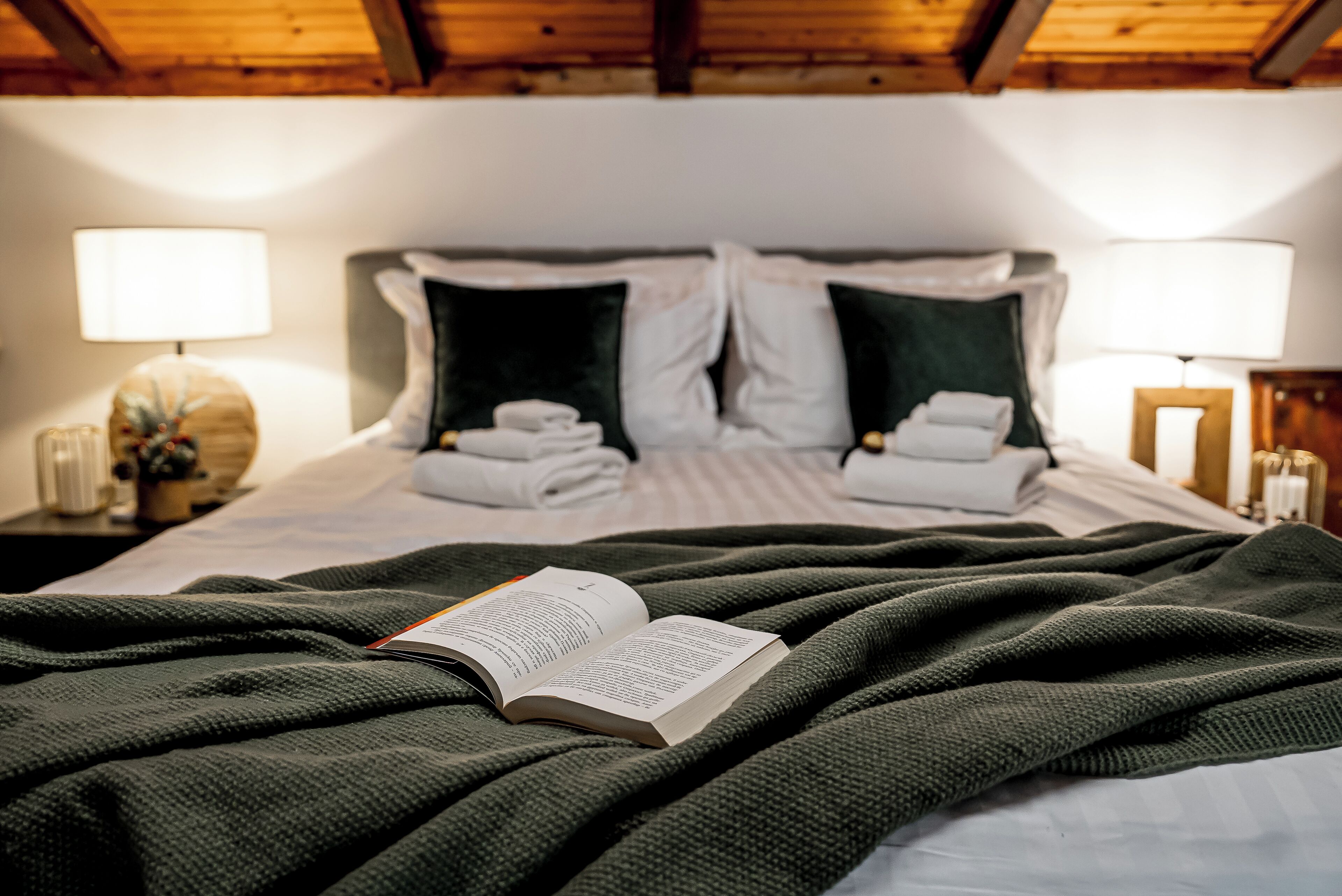 A neatly made bed with a green blanket, pillows, and a book open on the bed.